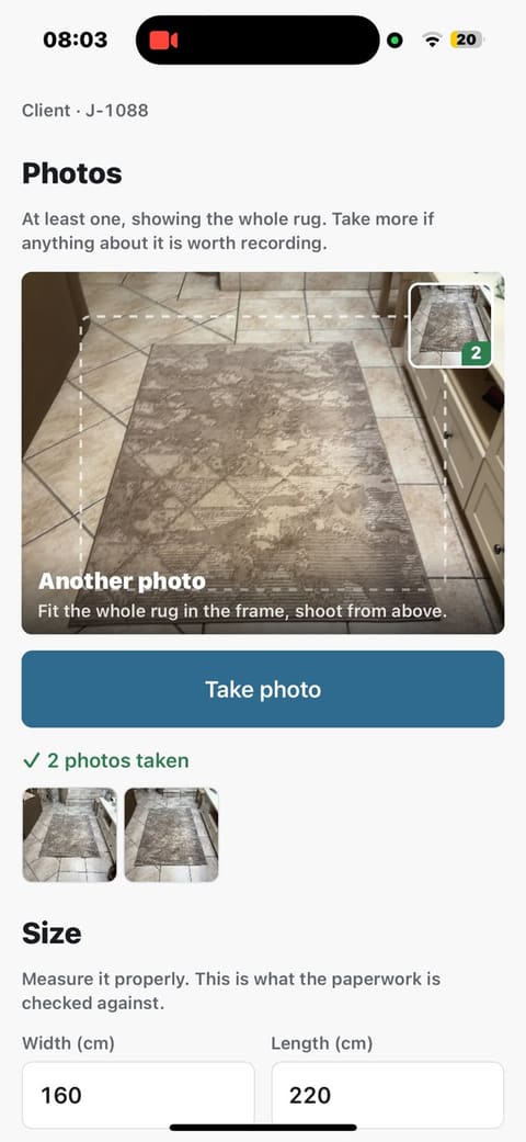 The photo step on a phone: a viewfinder framing a grey patterned rug on a tiled floor, a Take photo button, and a green tick reading '2 photos taken' above thumbnails of both shots.